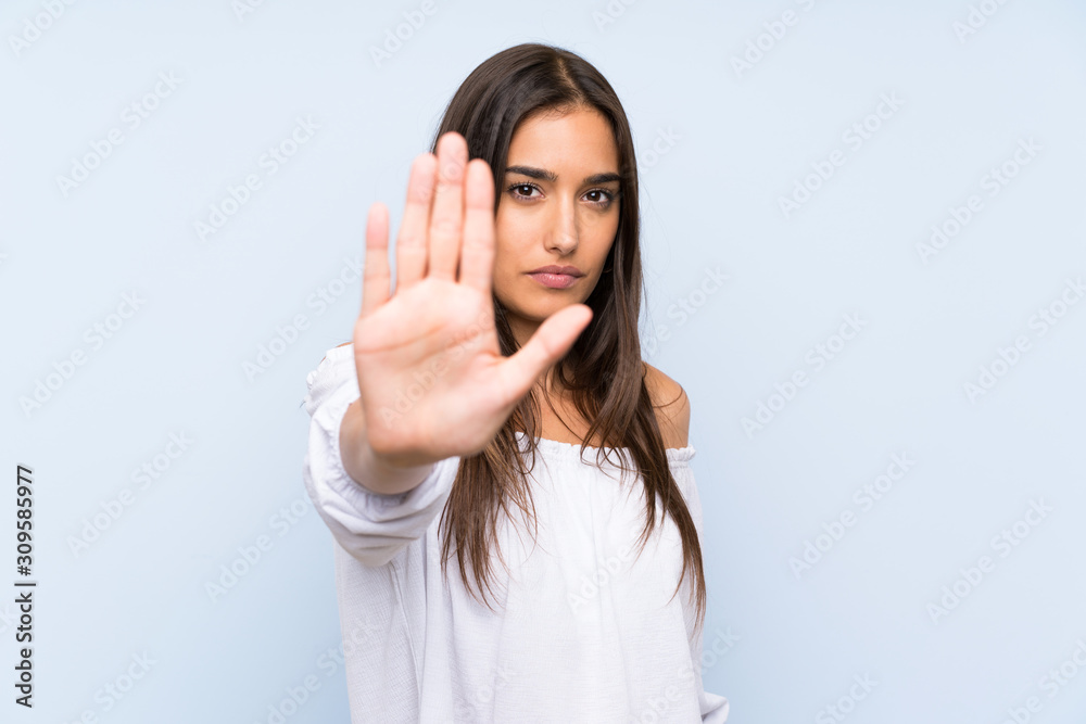 Young woman over isolated blue background making stop gesture with her hand Young woman over isolated blue background making stop gesture with her hand