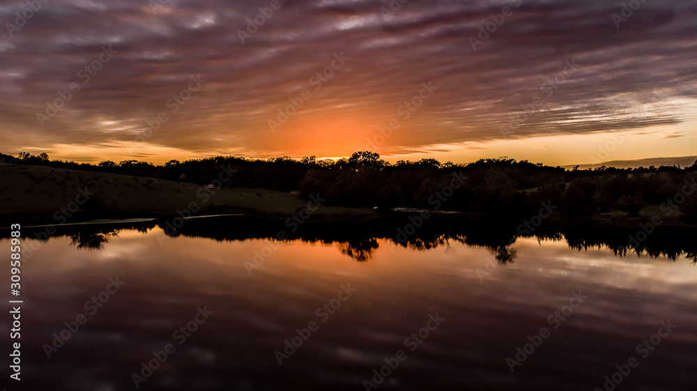Naklejka premium Golden hour sunset over a pond with clouds, sky, and trees
