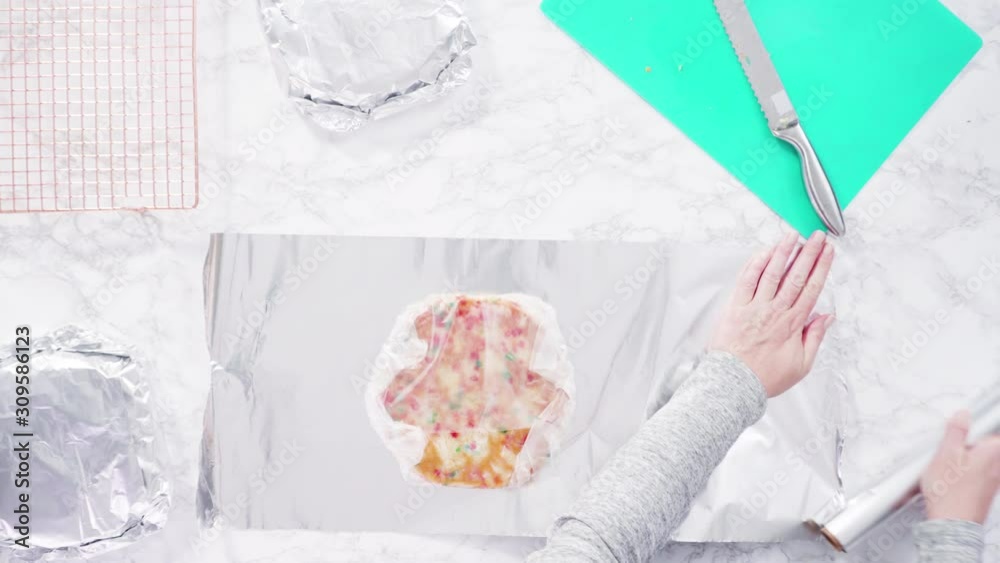 Flat lay. Step by step. Wrapping freshly baked funfetti cake into cellophane and cooking foil for freezer storage.