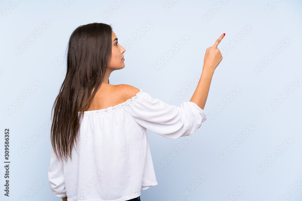 Young woman over isolated blue background pointing back with the index finger Young woman over isolated blue background pointing back with the index finger