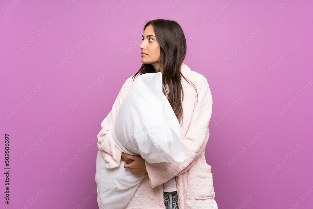 Young woman in pajamas and dressing gown over isolated purple background looking side