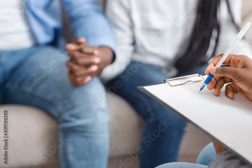 Marriage counselor taking notes during therapy session with black married couple