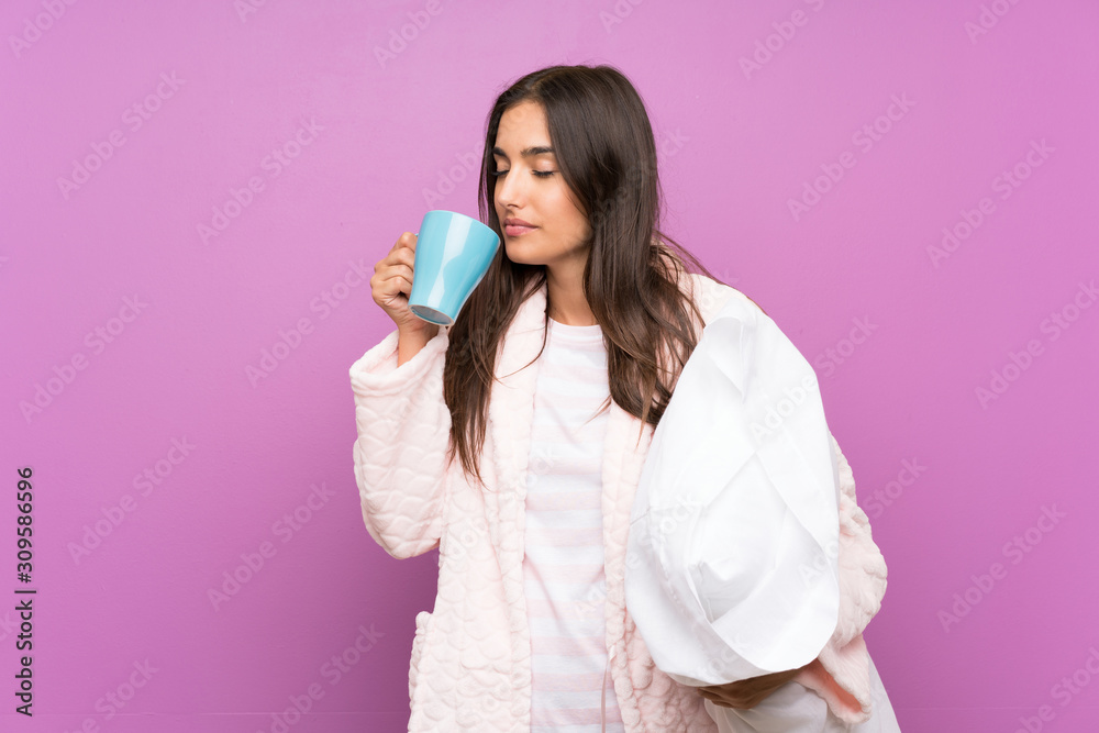 Young woman in pajamas and dressing gown over isolated purple background holding a cup of coffee Young woman in pajamas and dressing gown over isolated purple background holding a cup of coffee