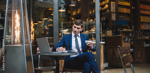 Young businessman with coffee cup writing on notebook