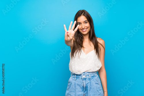 Fototapeta Young woman over isolated blue background happy and counting four with fingers