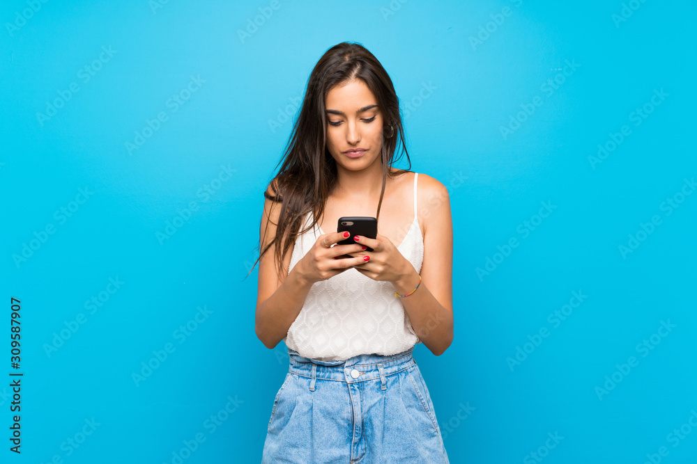 Young woman over isolated blue background sending a message with the mobile Young woman over isolated blue background sending a message with the mobile