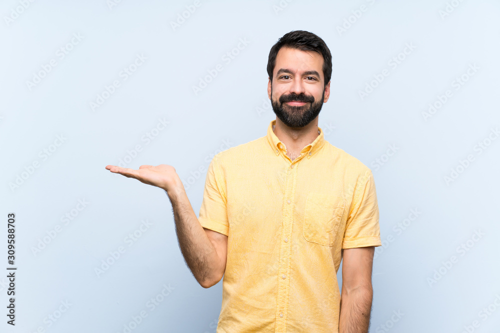 Young man with beard over isolated blue background holding copyspace imaginary on the palm to insert an ad Young man with beard over isolated blue background holding copyspace imaginary on the palm to insert an ad