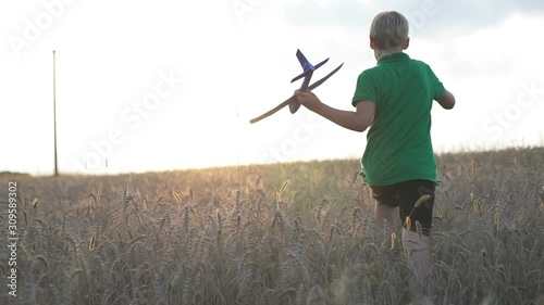 A boy with an airplane in his hands is running in the field