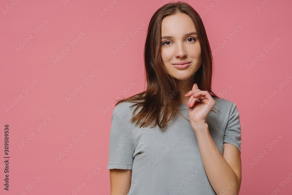 Obraz premium Confident lovely European woman has healthy pure skin, manicure, dressed in t shirt, enjoys photoshoot, models against rosy background with copy space, hears something pleasant or interesting