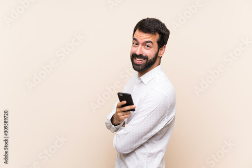 Young man with beard holding a mobile with arms crossed and looking forward © luismolinero