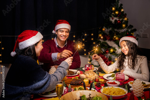 Happy family, father mother and daughter, having dinner together to celebrate Christmas holiday together, with sparkler light