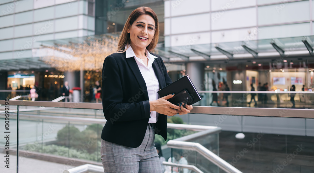 Smiling female with phone and notebook leaning on glass fence in mall Smiling female with phone and notebook leaning on glass fence in mall