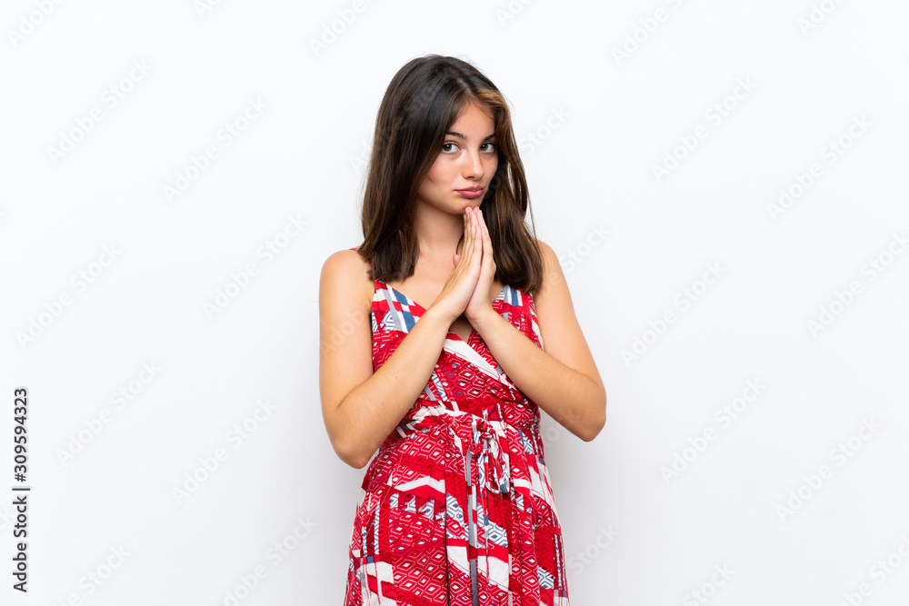 Caucasian girl in red dress over isolated white wall keeps palm together. Person asks for something Caucasian girl in red dress over isolated white wall keeps palm together. Person asks for something