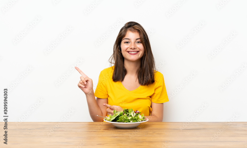 Caucasian girl with salad pointing finger to the side