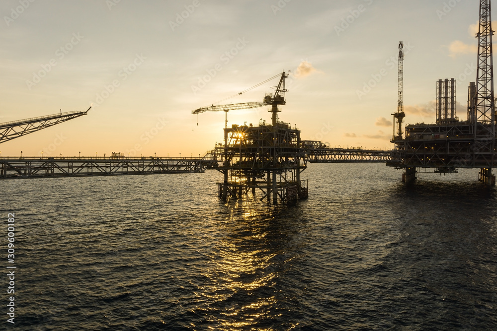 Silhouette of an oil production platform connected with a bridge at oil field during sunset