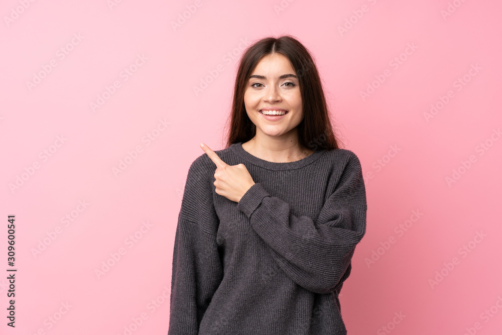 Young woman over isolated pink background pointing to the side to present a product