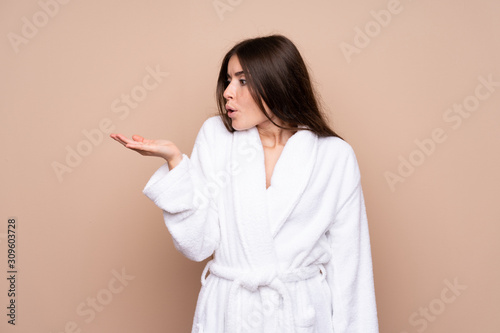Young girl in a bathrobe over isolated background holding copyspace imaginary on the palm