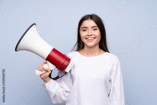 Young woman over isolated blue background holding a megaphone