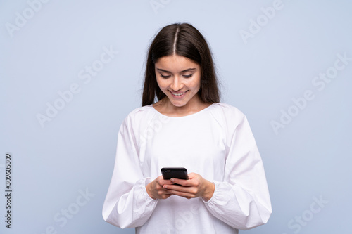 Young woman over isolated blue background sending a message or email with the mobile