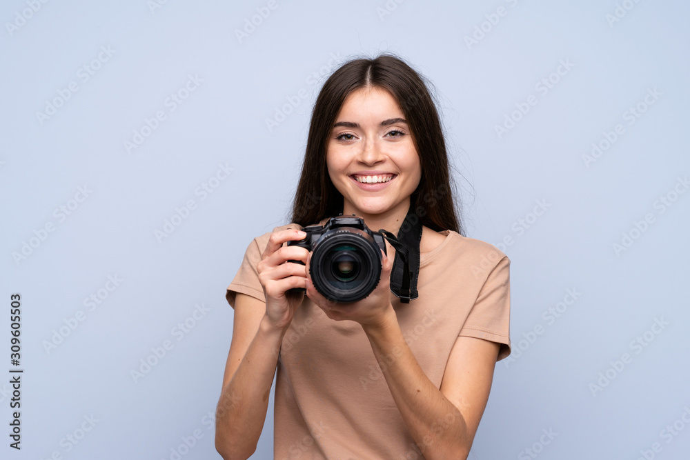 Young woman over isolated blue background with a professional camera