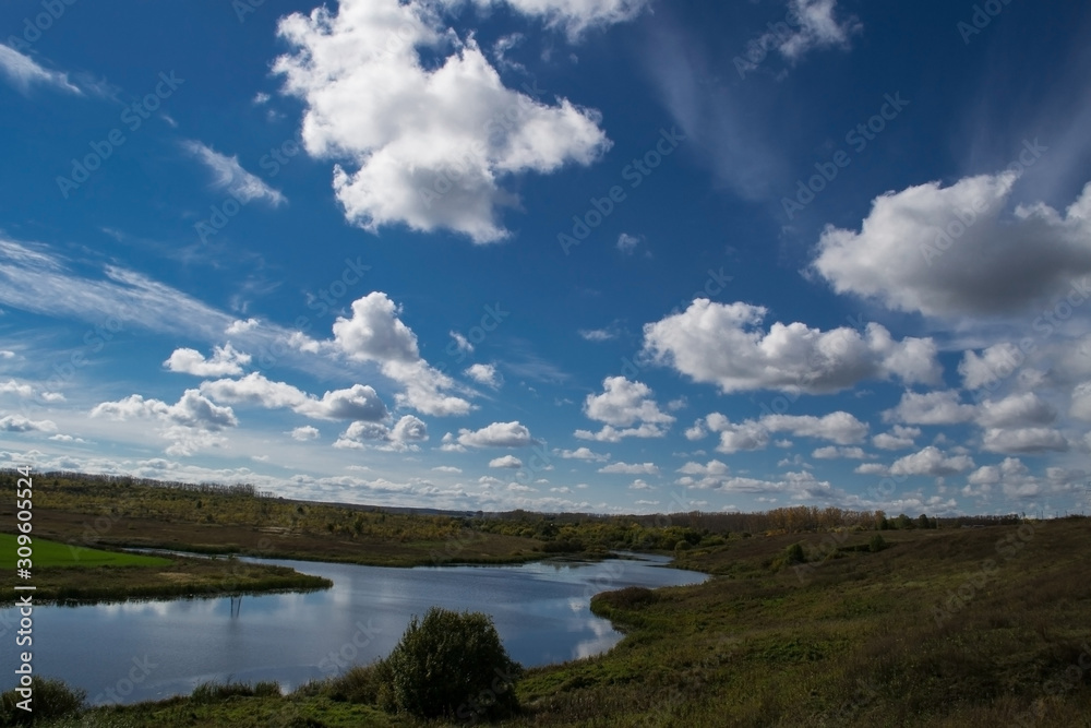  Blue sky with white cumulus clouds. Quiet river in a green valley.