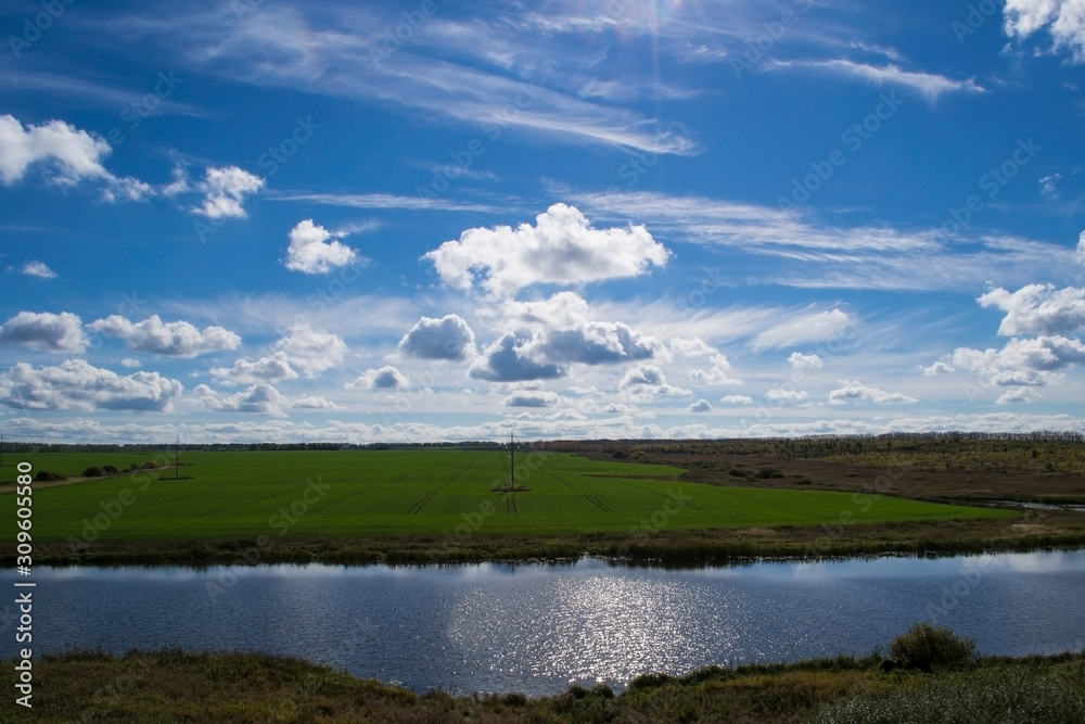 Blue sky with white cumulus clouds. Quiet river and green meadow.