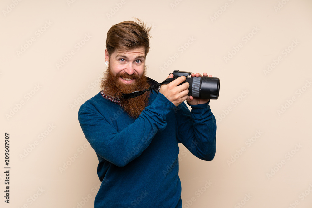 Redhead man with long beard over isolated background with a professional camera Redhead man with long beard over isolated background with a professional camera