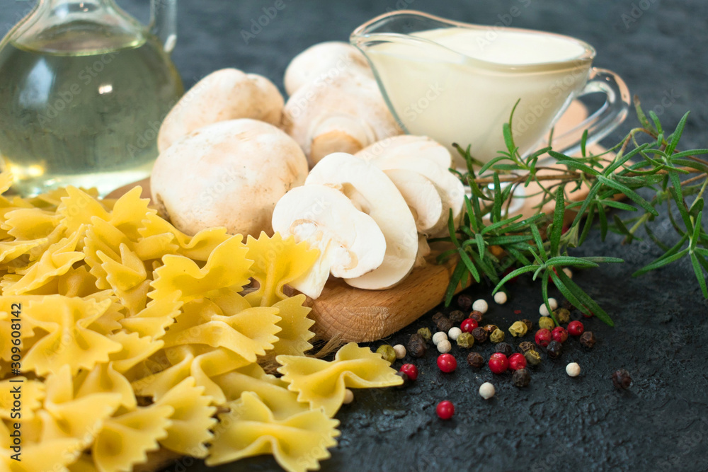 Ingredients for cooking pasta with mushrooms in a cream sauce on a black background. Close-up.