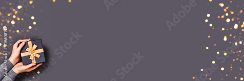 Christmas grey web-banner. Picture with woman's hands and gift box with loghts. Place for the text.
