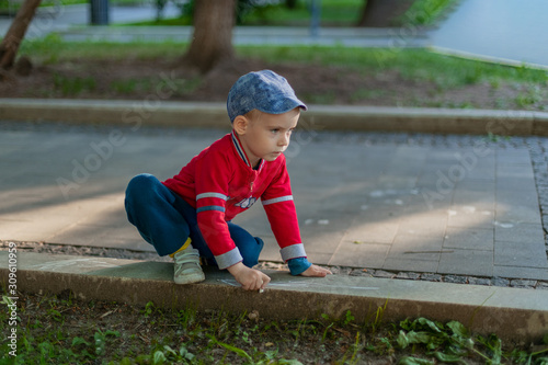 Fototapeta Naklejka Na Ścianę i Meble -  A child draws with chalk on the pavement in the park. Boy, border, red jacket, track, childhood, summer.