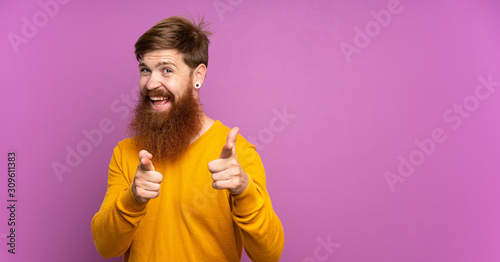 Redhead man with long beard over isolated purple background pointing to the front and smiling © luismolinero