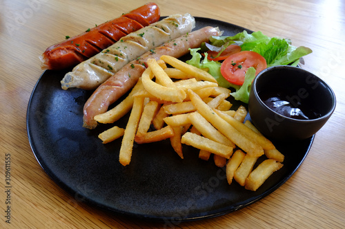 Meat sausages and French fries and fresh vegerable side dish served in black hot plate on wood dining table photo