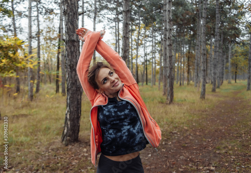 Young attractive sport woman in sportswear doing stretching exercise for hand in autumn forest. Warm up before jogging. Healthy lifestyle concept