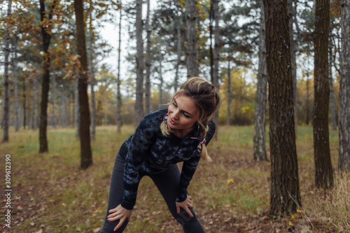 Tired sport fit woman with pigtails resting after jogging in the autumn forest. Healthy lifestyle concept