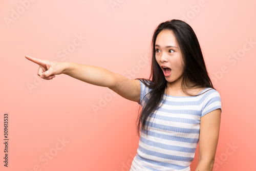 Teenager asian girl over isolated pink background pointing away