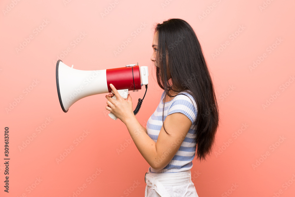 Teenager asian girl over isolated pink background shouting through a megaphone Teenager asian girl over isolated pink background shouting through a megaphone