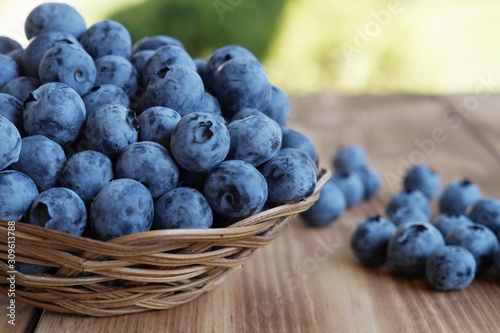 Ripe delicious blueberries close up in basket on wooden table with green blurred background P