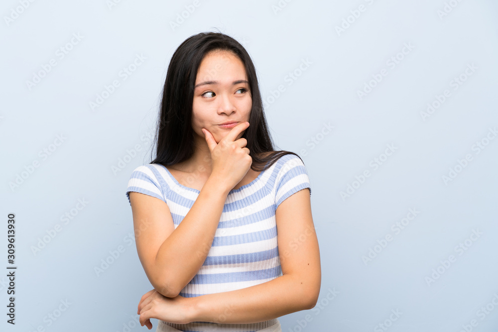 Teenager asian girl over isolated blue background thinking an idea Teenager asian girl over isolated blue background thinking an idea