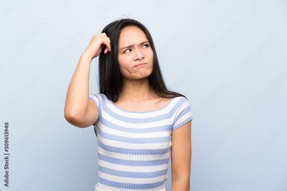 Teenager asian girl over isolated blue background having doubts and with confuse face expression Teenager asian girl over isolated blue background having doubts and with confuse face expression