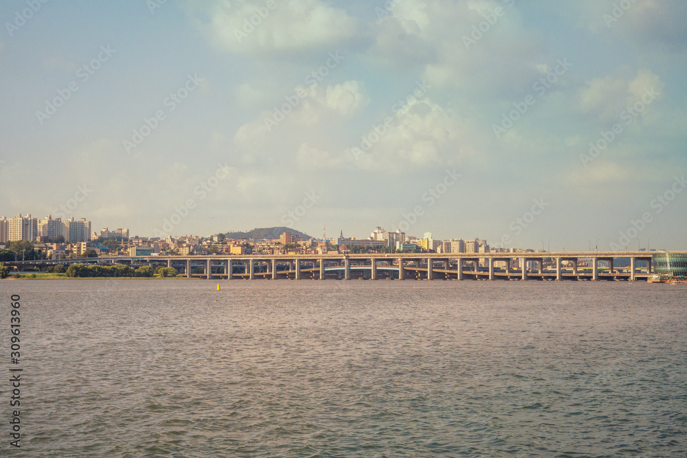 Long shot of river side oh Han River with double stories of bridge, houses, hills river and cloudy sky in Seoul, Korea