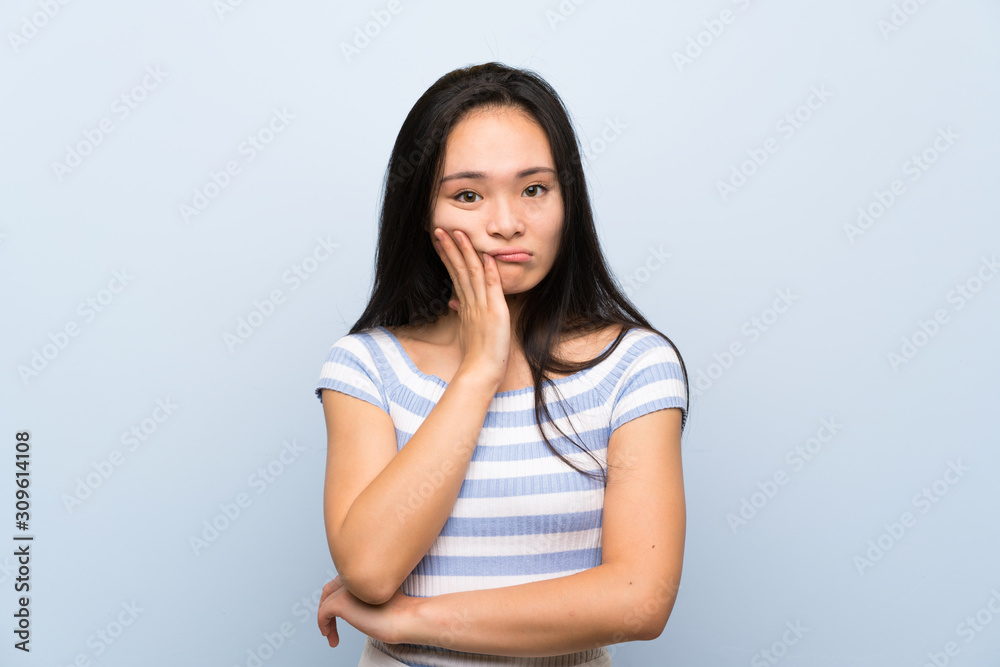 Teenager asian girl over isolated blue background unhappy and frustrated Teenager asian girl over isolated blue background unhappy and frustrated