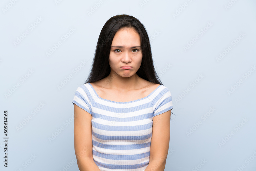 Teenager asian girl over isolated blue background sad Teenager asian girl over isolated blue background sad