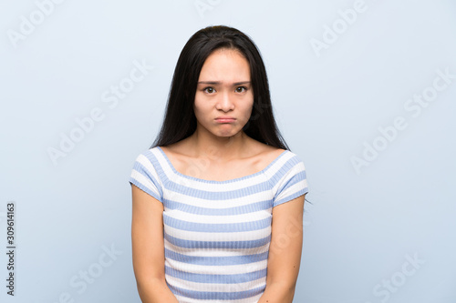 Teenager asian girl over isolated blue background sad