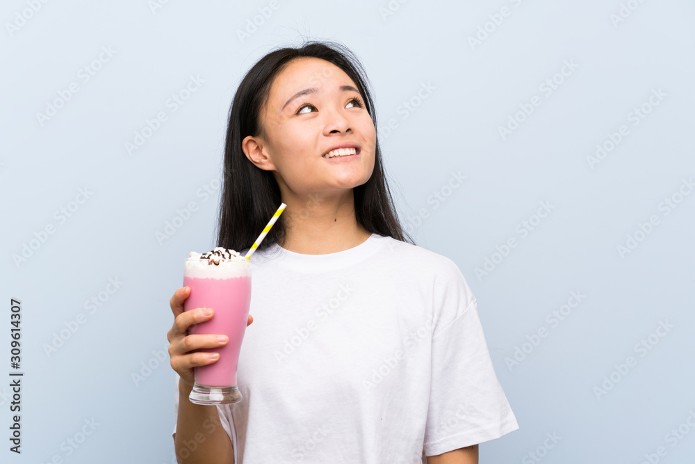 Teenager asian girl holding a strawberry milkshake looking up while smiling Teenager asian girl holding a strawberry milkshake looking up while smiling