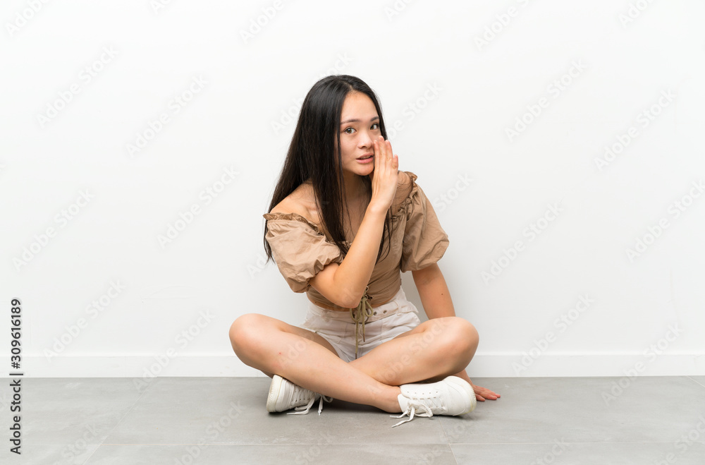 Teenager asian girl sitting on the floor whispering something Teenager asian girl sitting on the floor whispering something