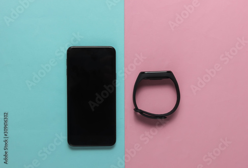 Smartphone and smart bracelet on pink blue pastel background. Modern gadgets. Top view. Minimalism