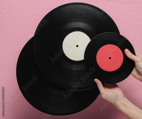 Female hands hold a vinyl record on a pink pastel background. Top view