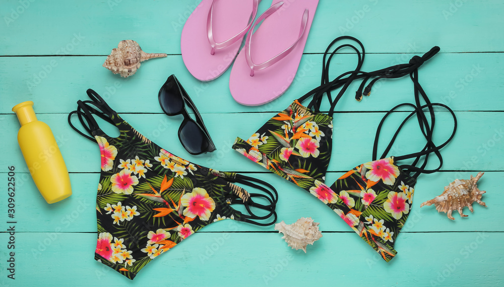 Obraz premium Summer fun background. Woman's swimsuit and beach accessories on blue wooden background. Overhead view of woman's swimwear. Vacation on the beach. Flat lay, top view.