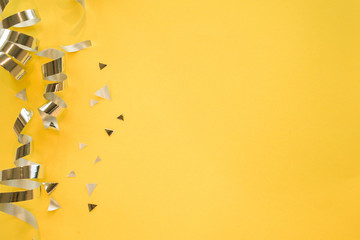 close up on group of silver color of rolling ribbon and confetti on yellow background with copy space for christmas festival happy new year ,carnival , birthday and anniversary, concept design