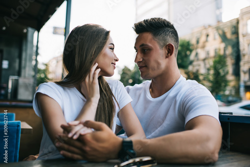 Lovely couple sitting together at street cafeteria looking at each other, positive girlfriend and boyfriend spending time together feeling happiness hugging, young romantic marriage resting outdoors
